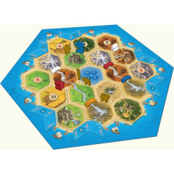 Tauler hexagonal de Catan amb peces de terrenys en verd, groc i marró, envoltat per una vora blava que simula el mar.