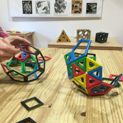 Magnetic Polydron: peces geomètriques de colors vibrants acoblades en estructures 3D sobre una superfície de fusta clara.