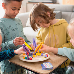 Niños jugando al ZigZag: juego de madera con base circular, palitos amarillos y morados, y pequeñas bolas de colores.