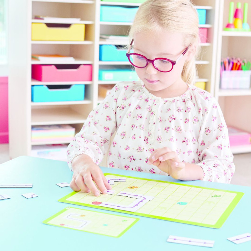 Tablero verde cuadriculado con pequeñas fichas de colores del juego Quadricoding Nathan sobre una mesa de trabajo.