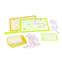 Juego educativo con tableros de rejilla amarillos y verdes, tarjetas de retos y pequeñas flechas rojas de plástico.