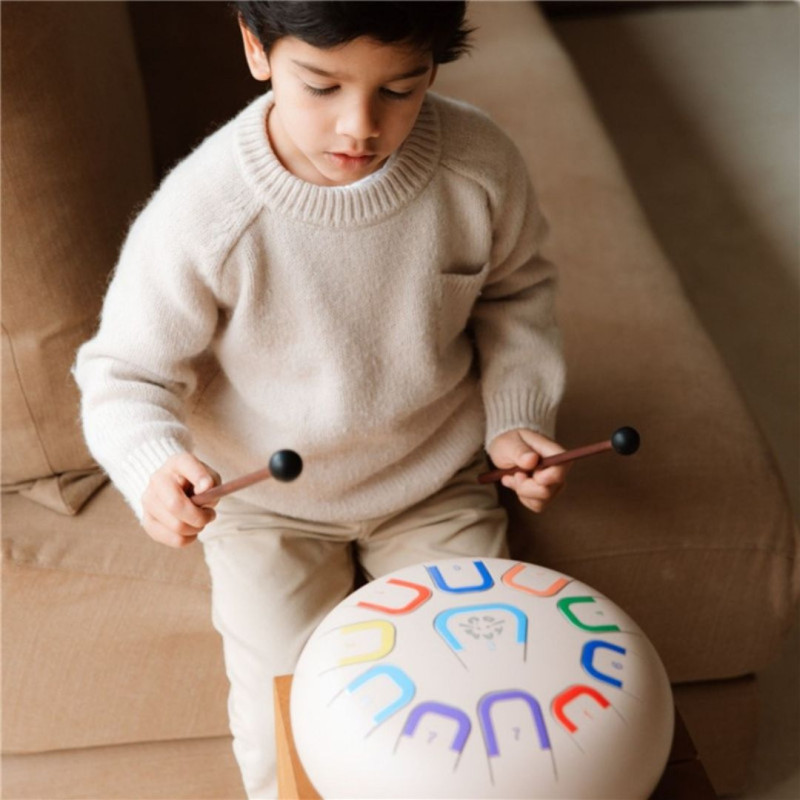 Tambor Tambú+ Soul Serenity blanco de 25cm con 11 notas de colores, tocado por un niño con baquetas de madera.