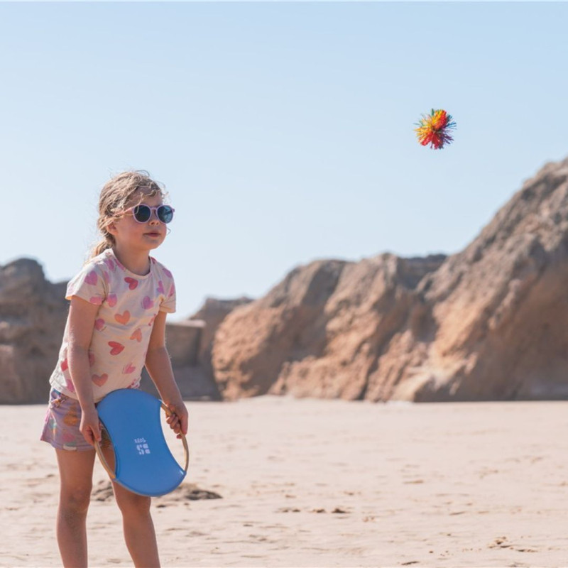 Raqueta de bambú azul con superficie de rebote y pelota naranja, ideal para jugar al aire libre en la playa.