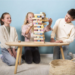 Tres niños juegan con una torre de 48 bloques de madera clara con números impresos sobre una mesa de madera natural.