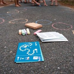 Set de jocs amb guixos de colors, manual d'instruccions blau i caixa de cartró a terra amb cercles blancs traçats.
