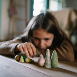 Niña manipulando árboles de madera pintados a mano en tonos verdes y rosas, con formas cónicas y redondeadas suaves.