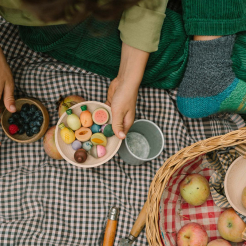 Set de fruites de fusta Grapat de colors vibrants i formes arrodonides per a joc simbòlic sobre unes estovalles de pícnic.